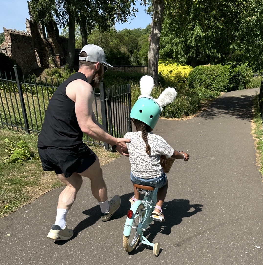 Andy running alongside his daughter as she learns to ride her bike