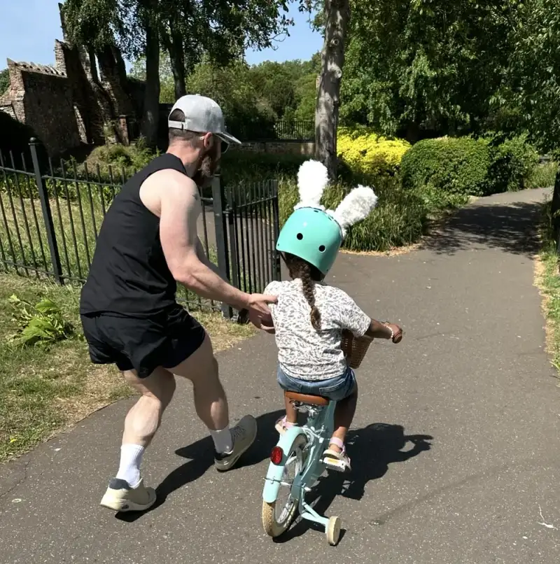Andy running alongside his daughter as she learns to ride her bike